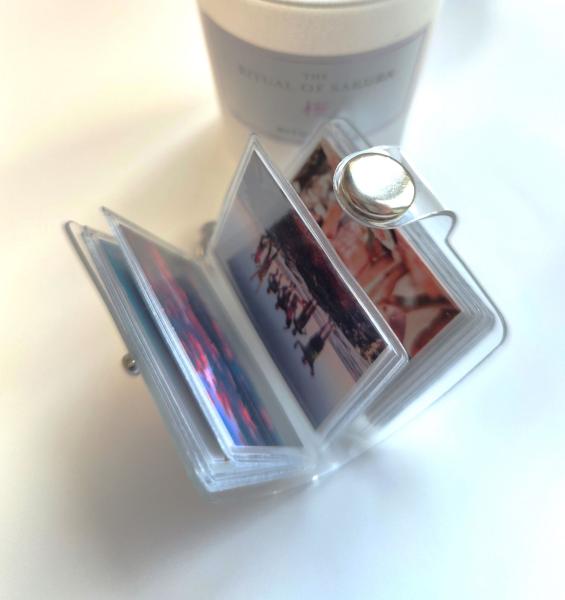 Offenes Mini-Fotobuch-Schlüsselanhänger mit mehreren Bildern, darunter ein Bild einer Gruppe von Menschen am Strand und ein Sonnenuntergangsfoto. Im Hintergrund ist eine Rituals-Kerze zu sehen.
